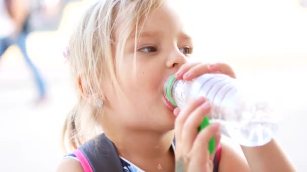 Het kind blond meisje met plezier drinkwater buitenshuis. Een kind is het drinken van zuiver water uit een fles — Stockvideo