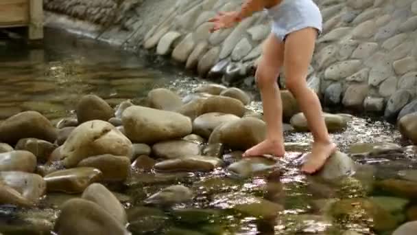 Una niña pequeña cruza un arroyo sobre las rocas descalza — Vídeos de Stock