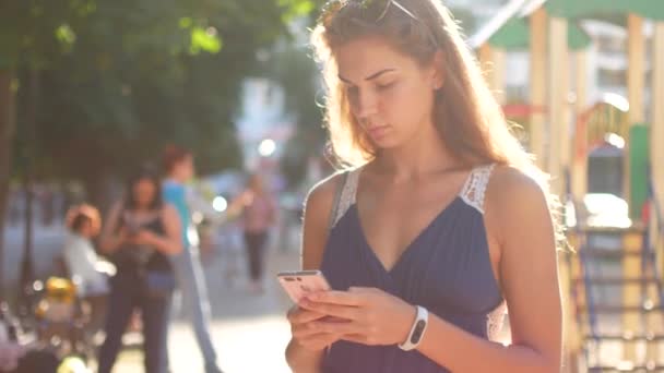 Привлекательная молодая женщина, гуляющая по солнечным улицам города и общающаяся с друзьями, радостная хипстерша, пользующаяся мобильным телефоном на открытом воздухе, закатный фон — стоковое видео