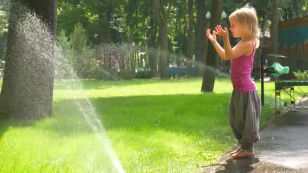 Malá holčička v parku pod kapkami zalévání pad — Stock video