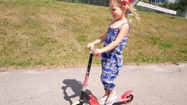 Küçük kız hızlı tekme scooter yaz ülke yan Park yol boyunca sürmek. Ağır çekim