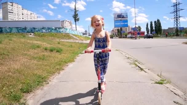 Malá holčička rychle jede koloběžka podél cesty v létě země straně parku. Zpomalený pohyb — Stock video