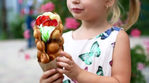 Een kleine prachtig meisje is het eten van wafels met fruit en ijs. Het zomerterras — Stockvideo