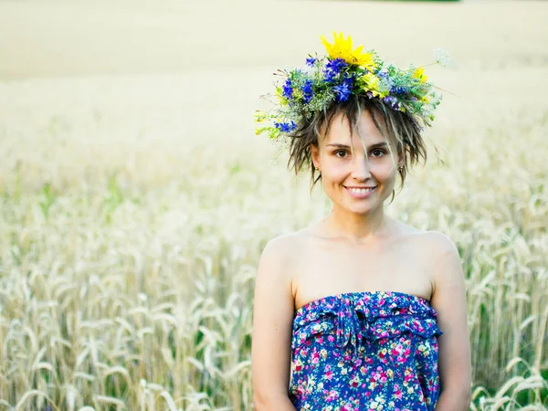 Porträt einer jungen Frau in einem Kranz aus Wildblumen steht bei Sonnenuntergang auf dem Feld. — Stockfoto