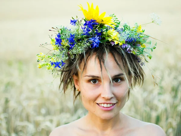 Porträt einer jungen Frau in einem Kranz aus Wildblumen steht bei Sonnenuntergang auf dem Feld. — Stockfoto