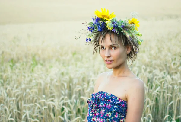 Porträt einer jungen Frau in einem Kranz aus Wildblumen steht bei Sonnenuntergang auf dem Feld. — Stockfoto