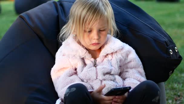 Маленька дівчинка дивиться мультфільми по телефону — стокове відео