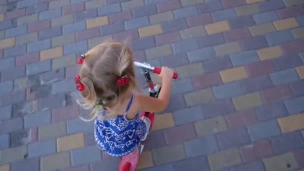 Una bambina bionda cavalca rapidamente uno scooter. Contesto urbano — Video Stock