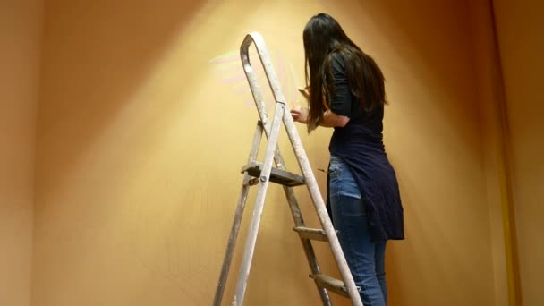 Girl artist paints a wall standing on a ladder — Stock Video