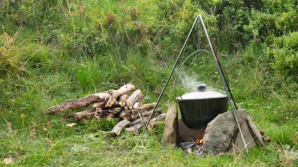 Cooking outdoor food in tourist pot at bonfire. Process preparing camping food on burning fire while hiking to wild nature — Stock Video