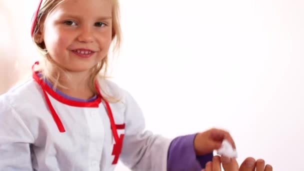 La niña bonita está tratando de ser doctora. Un niño en el traje de un médico cura una pierna a su madre — Vídeo de stock