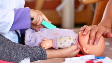 Etkin bir küçük okul öncesi çocuk, sarı saçlı, oldukça küçük bir kız onu bebeklerle oynar. Doktor oynayan
