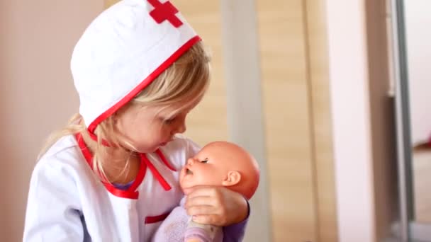 La niña está jugando al doctor. Un niño en un traje de médico calma a una muñeca de juguete — Vídeo de stock