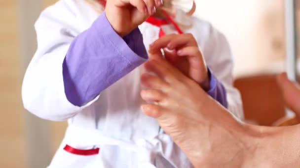 Sevimli küçük kız doktor olmaya çalışıyor. Bir çocuk bir doktor elbiseli bir bacak da annesinin iyileştiriyor — Stok video
