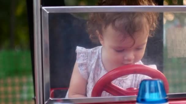 Niña y monta un coche eléctrico en el parque para el entretenimiento. Atracciones para niños. Zona de juegos — Vídeos de Stock