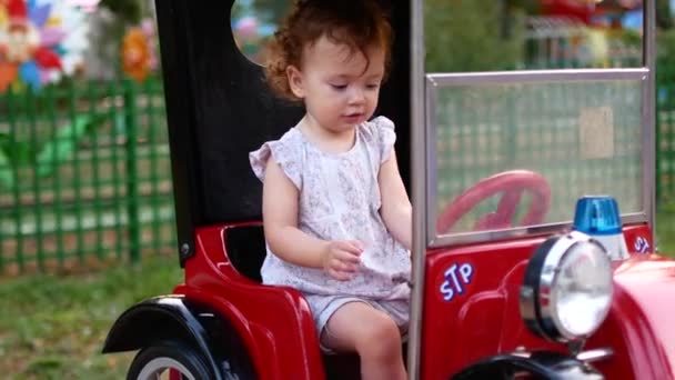 Niña y monta un coche eléctrico en el parque para el entretenimiento. Atracciones para niños. Zona de juegos — Vídeos de Stock