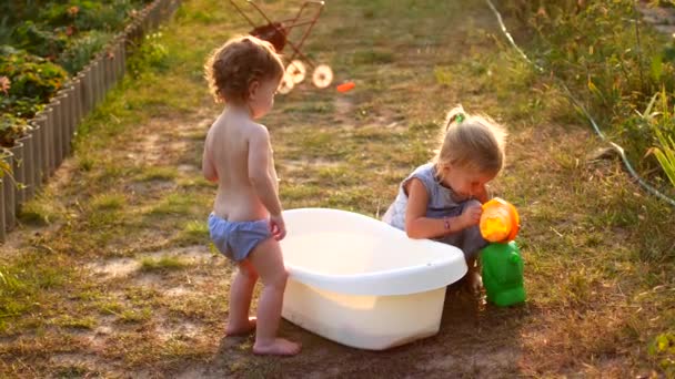 Crianças alegres felizes brincando com água nas férias de verão. Bonito adorável sorrindo crianças pulverizando com uma mangueira de jardim no quintal. Fechar — Vídeo de Stock