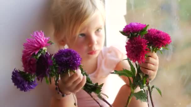 De jonge ballerina zit op het venster en houdt van bloemen in haar handen — Stockvideo