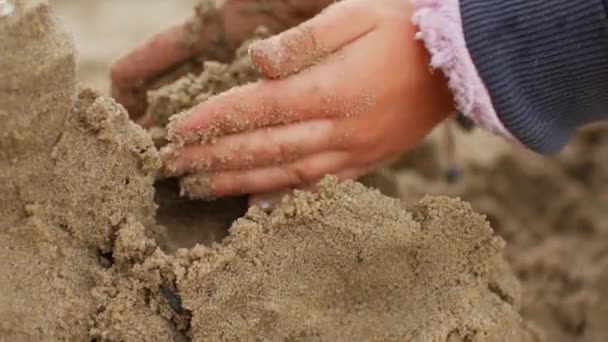 Niños jugando a la arena en la playa. Niña construye castillo de arena por sí mismo en la playa . — Vídeos de Stock