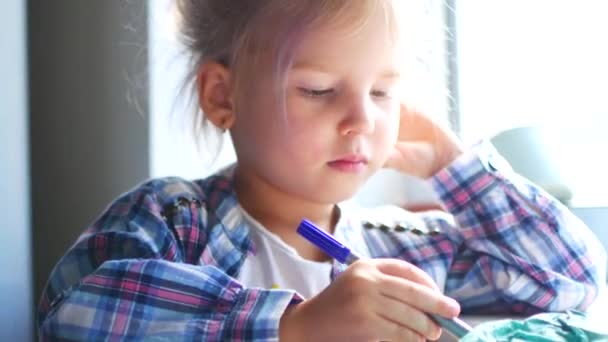 Linda niña se sienta a su mesa y dibuja con lápices de colores . — Vídeo de stock