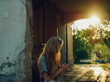 Günbatımı ışınlarının Kızıl saçlı Genç kız telefonda bir ileti yazar.