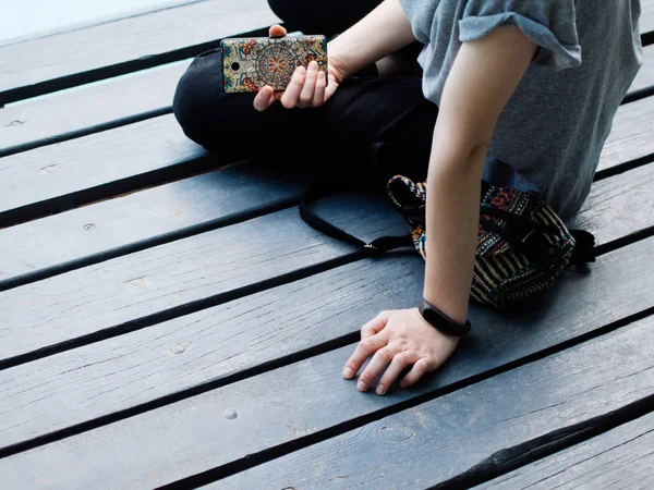 Retrato de la joven hermosa chica rubia sonriente usando Smartphone mientras está sentada en el puente . Fotos De Stock Sin Royalties Gratis