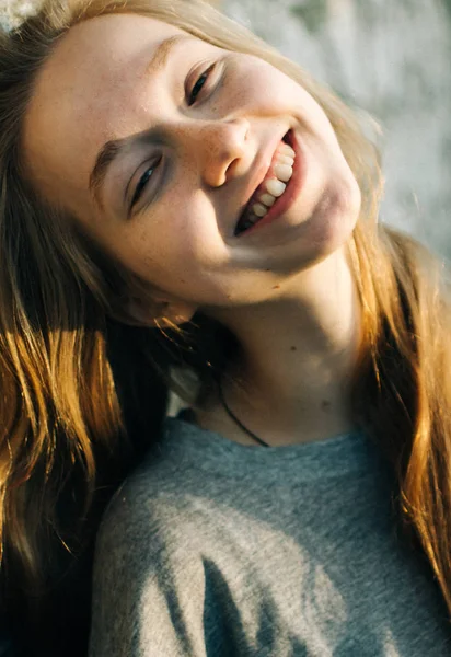 Retrato de una hermosa adolescente apoyada en una pared de piedra texturizada al aire libre, mirando sonriente a la cámara . Imagen De Stock