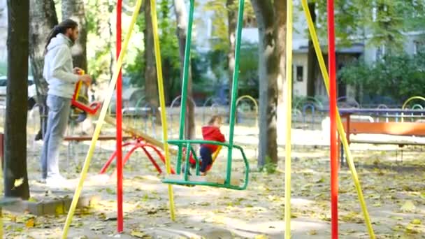 Familia feliz joven con pequeño bebé en el patio de recreo para niños — Vídeo de stock