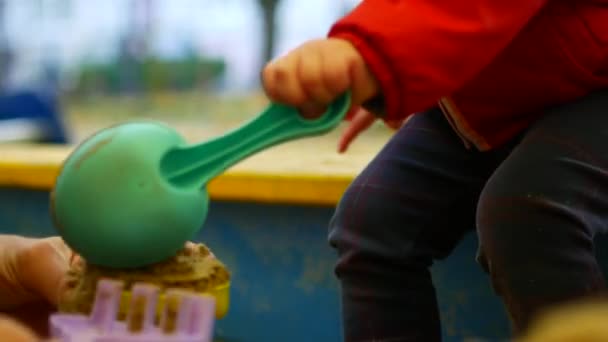 Het kind raakt de zand beeldjes met zijn hand. Close-up. Het meisje speelt in de zandbak. — Stockvideo