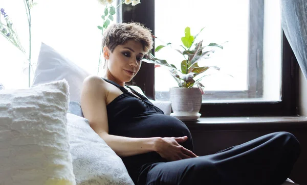 La futura madre si siede su un letto. La donna incinta, in un vestito nero — Foto Stock