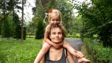 mutlu anne güzel küçük kızın onun omuzlarında taşıyan, çocuk ile parkta yürümek,