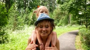 mutlu anne güzel küçük kızın onun omuzlarında taşıyan, çocuk ile parkta yürümek,