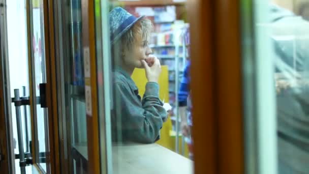 Junge attraktive Frau mit Hut, die an der Fast-Food-Theke auf sein Essen wartet. Blick durch Glas. — Stockvideo