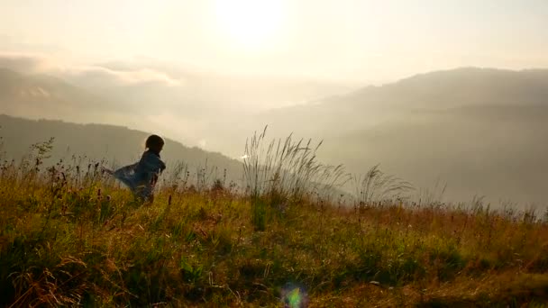 Uma criança está se divertindo no fundo de um pôr do sol nas montanhas. Uma manhã enevoada — Vídeo de Stock