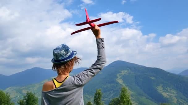 Joven mujer bonita de nuevo a la cámara y mantiene el modelo rojo del avión en ruach. concepto de viaje y libertad . — Vídeo de stock