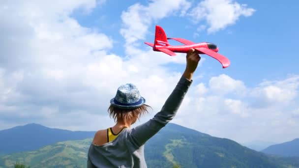 Junge hübsche Frau zurück in die Kamera und hält das rote Modell des Flugzeugs in Ruach. Konzept von Reisen und Freiheit. — Stockvideo