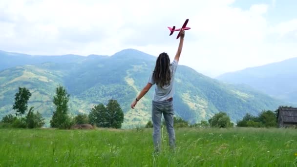 En ung man med dreadlocks leker med ett modellflygplan i bergen — Stockvideo