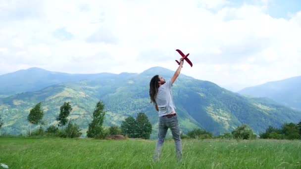 Ein junger Mann mit Dreadlocks spielt mit einem Modellflugzeug in den Bergen — Stockvideo