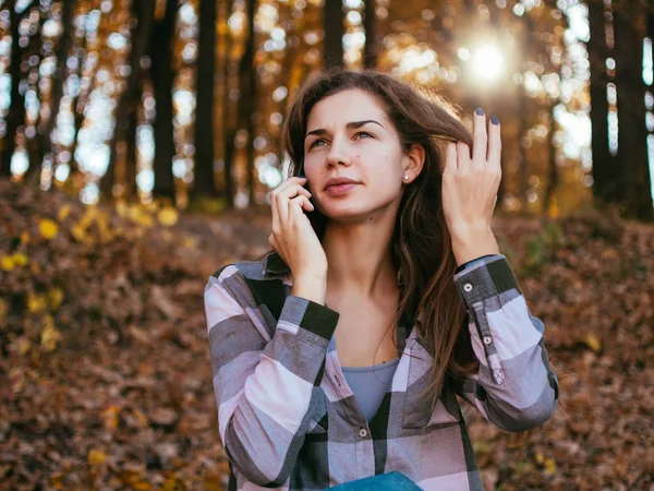 秋の森の背景に携帯電話で話している若い白人の女の子 — ストック写真