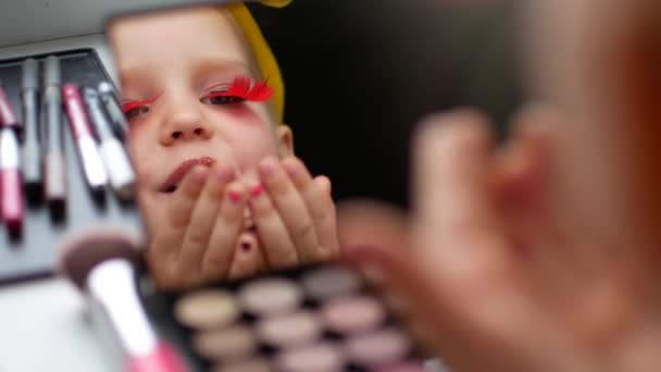Een mooi klein meisje in de spiegel maakt zelf een make-up — Stockvideo
