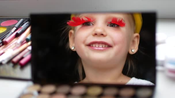 Een mooi klein meisje in de spiegel maakt zelf een make-up — Stockvideo