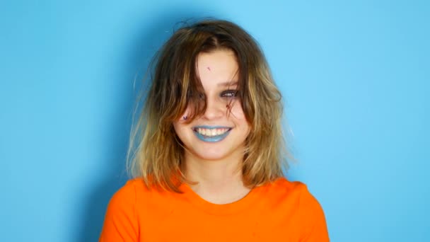 Happy girl with long hair laughing and keeping hands at her face while standing in indoors of isolated over blue background. Portrait of beautiful surprised and shocked teen girl Emotion, lifestyle — Stock Video