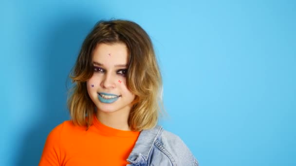 Chica feliz con el pelo largo riendo y manteniendo las manos en su cara mientras está de pie en el interior de aislado sobre fondo azul. Retrato de hermosa chica adolescente sorprendida y conmocionada Emoción, estilo de vida — Vídeos de Stock