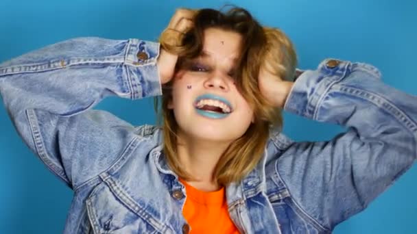 Happy girl with long hair laughing and keeping hands at her face while standing in indoors of isolated over blue background. Portrait of beautiful surprised and shocked teen girl Emotion, lifestyle — Stock Video