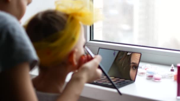 A casa, in camera da letto, madre e figlia giocano e si truccano. La madre e la figlia sorridono mentre provano i trucchi di bellezza. Concetto: bellezza, famiglia, divertimento, ricordi . — Video Stock