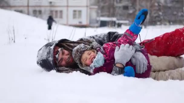 Guapo padre joven y su pequeña hija linda se divierten al aire libre en invierno. Disfrutando pasar tiempo juntos mientras hacen ángeles de nieve. Concepto familiar — Vídeos de Stock