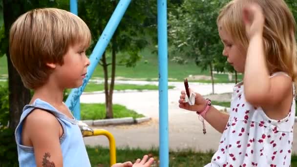 Vänner äta choklad i parken. Flickan delar med pojken — Stockvideo