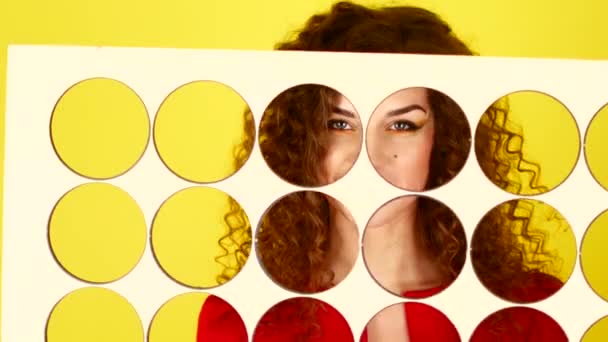 Curly flicka i en röd klänning på gul bakgrund. Tittar in i kameran genom skärmen. 4k. — Stockvideo