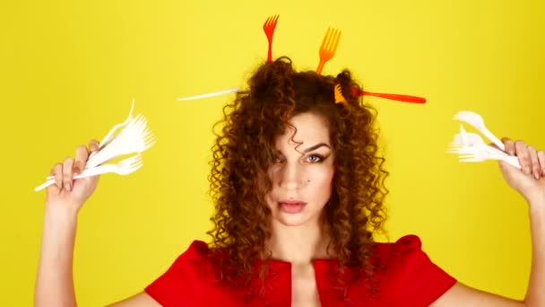 Joven mujer hermosa en un vestido rojo sobre un fondo amarillo. Retrato femenino con tenedores de plástico en el cabello. Concepto de protección medioambiental . — Vídeo de stock