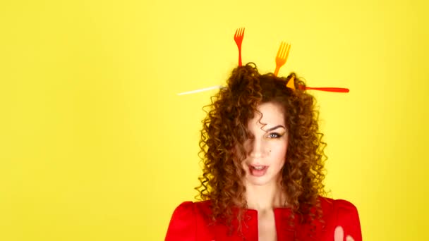 Joven mujer hermosa en un vestido rojo sobre un fondo amarillo. Retrato femenino con tenedores de plástico en el cabello. Concepto de protección medioambiental . — Vídeo de stock